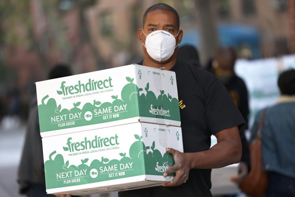 Erik Cliette wearing a mask, carrying FreshDirect food boxes for distribution in Harlem, highlighting food insecurity in New York City