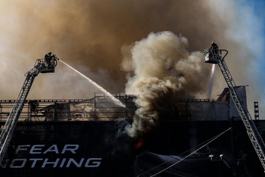 Firefighters trying to extinguish a large fire at the historic Boersen stock exchange building in central Copenhagen, Denmark, with the building's landmark spire collapsing amid the flames.