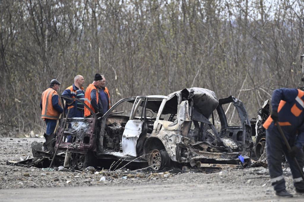 Four men wearing orange vests look over a burned out car Saturday after Russian attacks on Kharkiv, Ukraine.