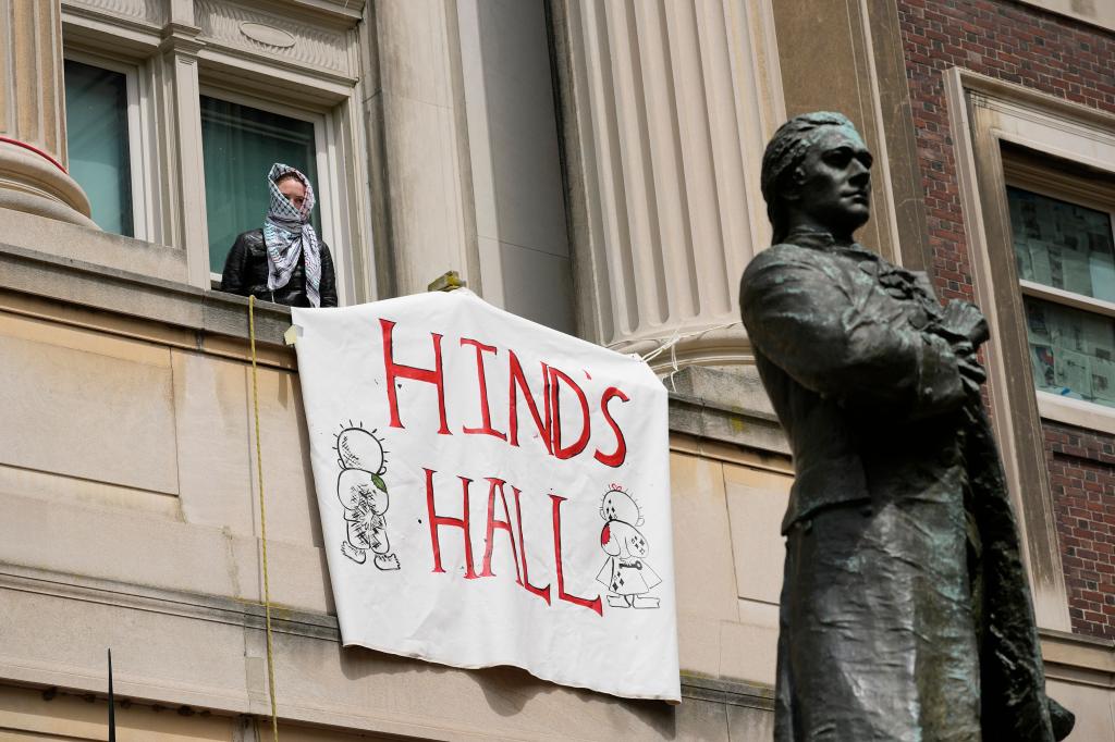 Pro-Palestine student protestors peering out from Hamilton Hall at Columbia University, barricaded inside in protest of the war in Gaza, holding a sign, 2024.