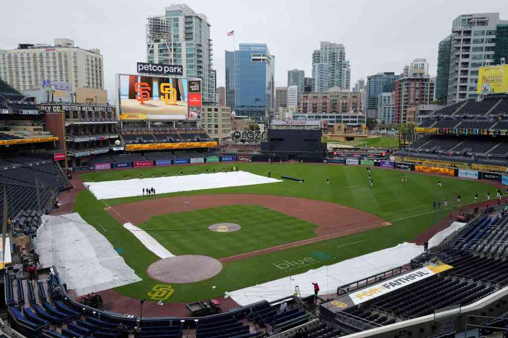 The grounds crew lifts the tarp after the rain has stopped before the game between the San Diego Padres and the San Francisco Giants at Petco Park on March 30, 2024. 