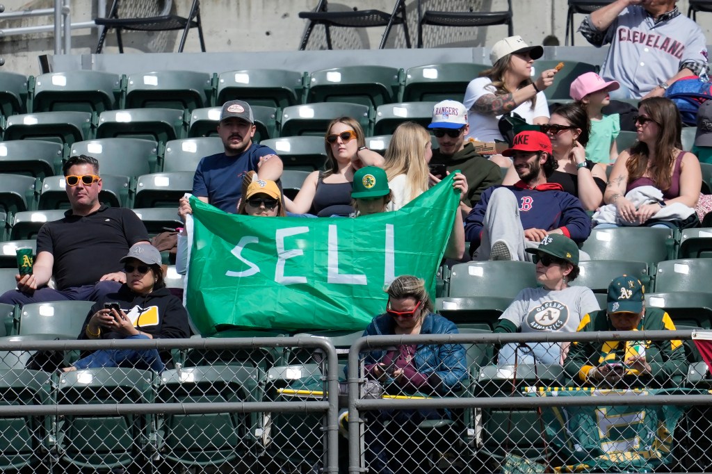 Fans hold up a sign calling for Oakland Athletics management to sell the team