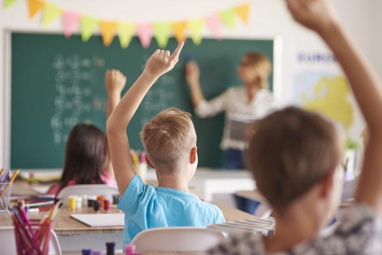 A group of children raising their hands in a classroom