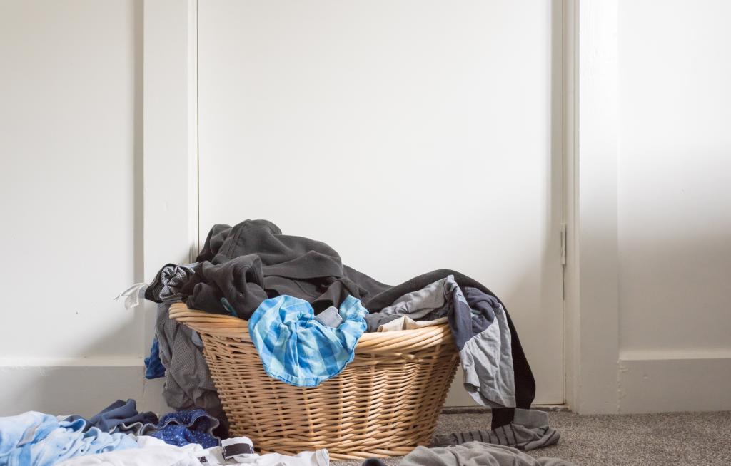 Low angle view of overflowing wicker basket with blue and black clothes against a white wall