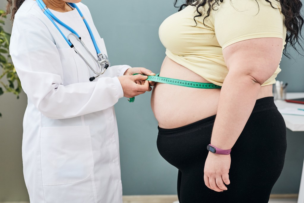 A nutritionist measuring a woman's waist with a tape to assess obesity and prescribe a weight loss diet