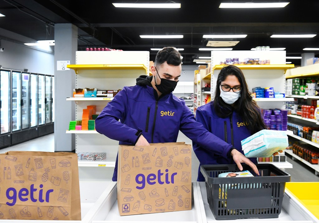 Order pickers working in a Getir dark store, wearing face masks and standing next to a box, in Amsterdam city centre