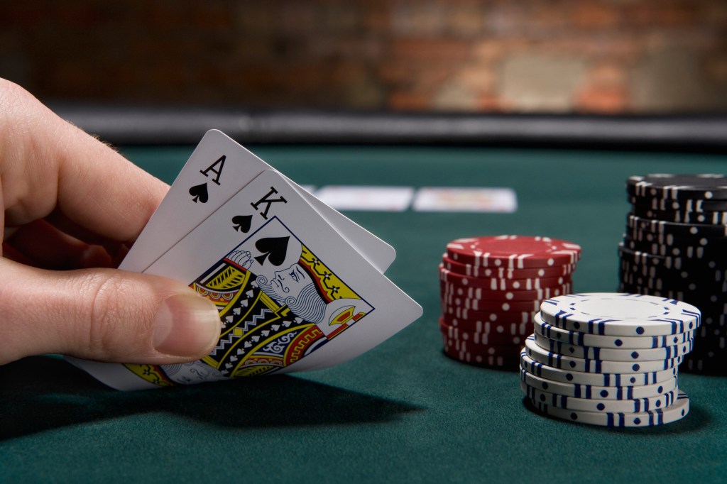 a poker player showing two of their cards to the camera (an ace and king of spades) with poker chips on the table