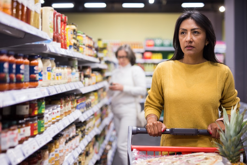 Hispanic woman thoughtfully pushing a shopping trolley in a grocery store