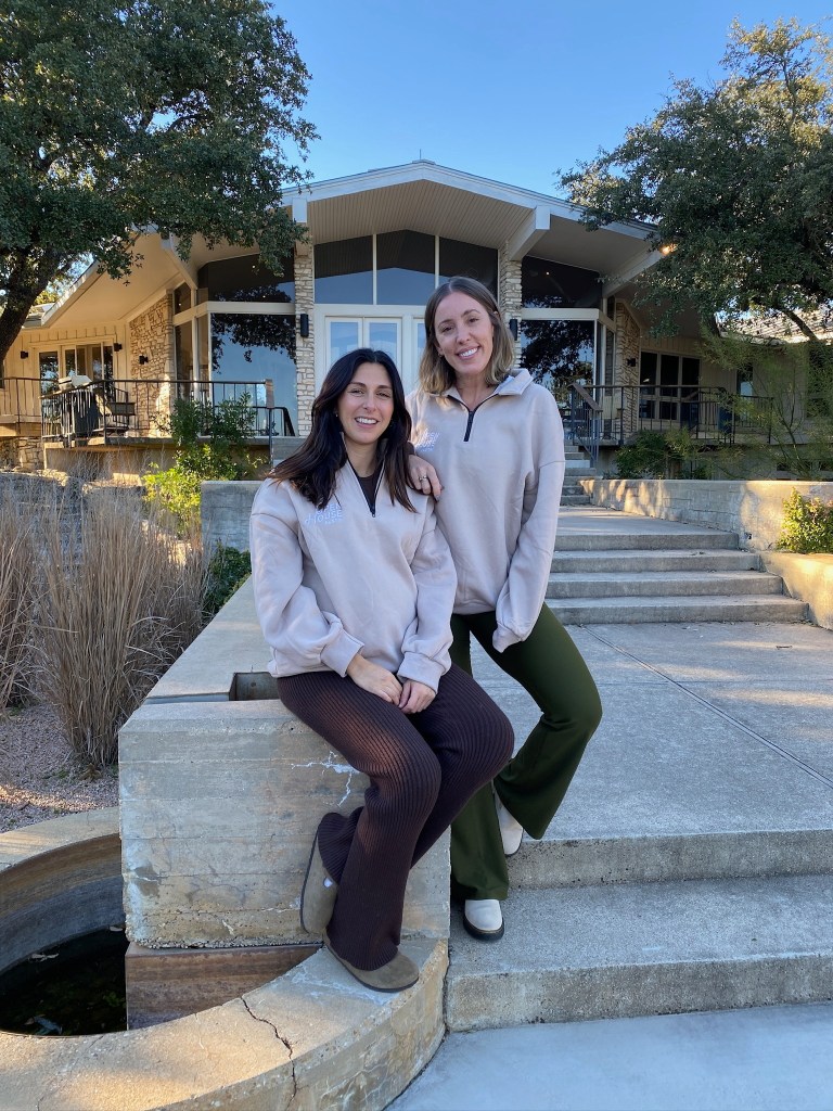 Real estate experts Kristina Modares and Stephanie Douglass sitting on a concrete ledge, advocating for buying houses with friends