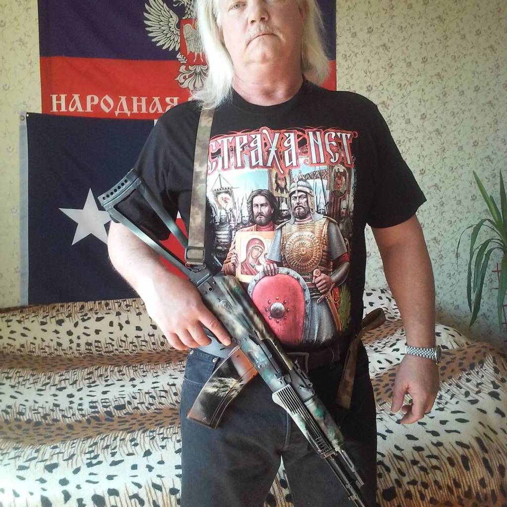 Russell Bentley poses with a gun in front of a bed covered with a leopard-patterned spread.