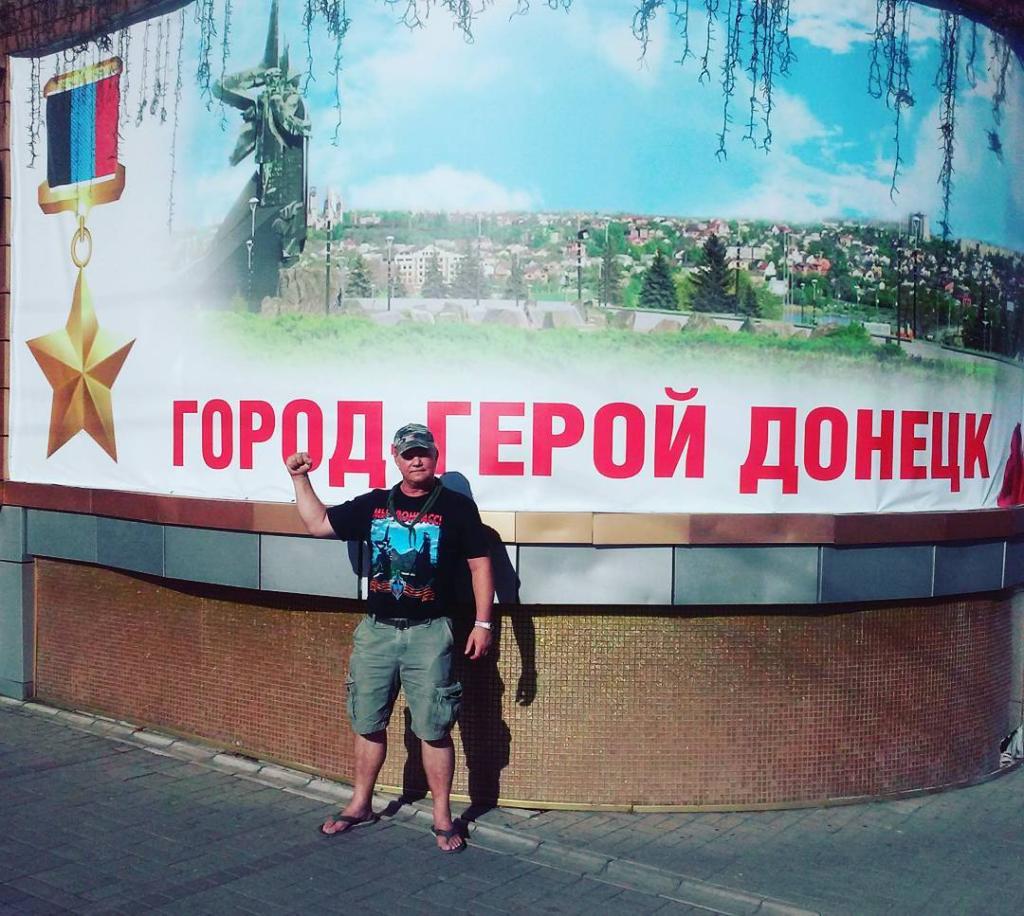 Russell Bentley, dressed in shorts and a t-shirt, poses in front of a billboard in Ukraine.