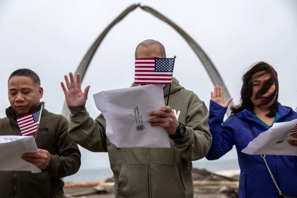 Immigrants take the oath of allegiance to the United States during a naturalization ceremony held in front of the "Gateway to the Arctic" whale bone sculpture on Aug. 9, 2023.