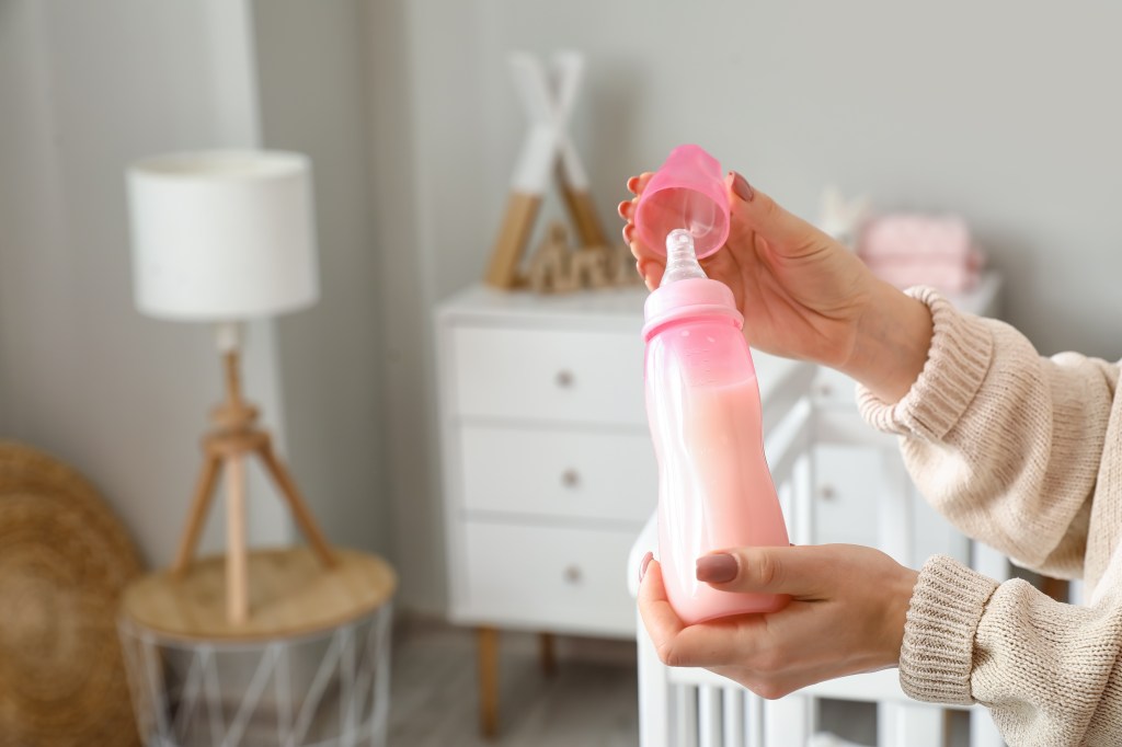 Woman holding a bottle of milk for a baby in a room