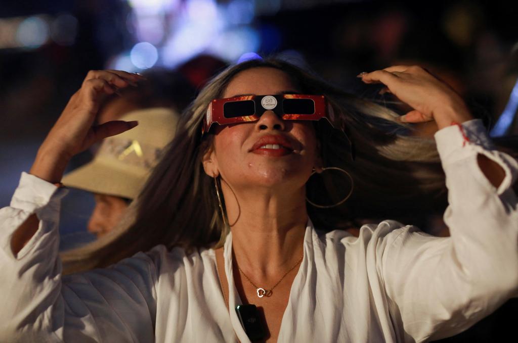 A woman demonstrates how to use special protective glasses to observe the solar eclipse, before handing them out to tourists and residents at the Malecon, two days ahead of a total solar eclipse in Mazatlan, Mexico April 6, 2024. 