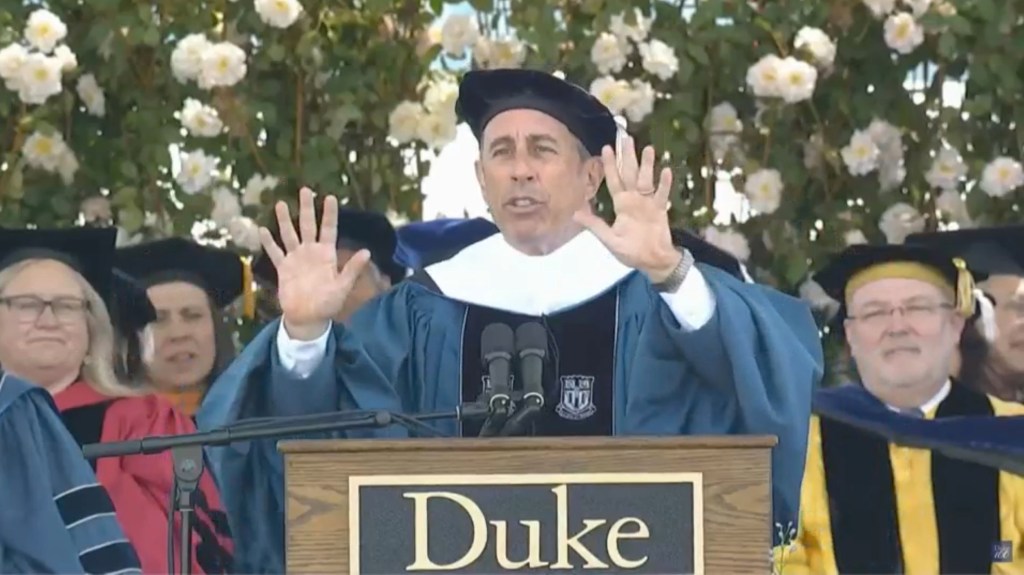 Jerry Seinfeld, in cap and gown, at a podium