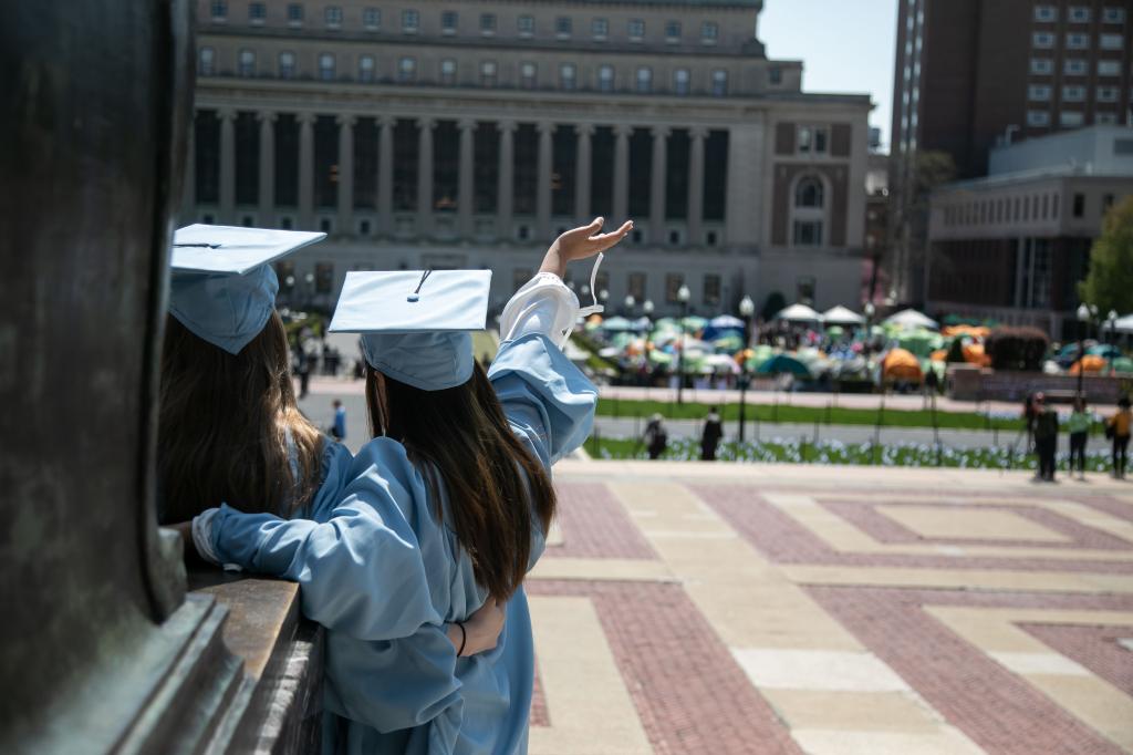 A group of students in blue graduation gowns posing for photos amidst an anti-Israel demonstration at the Gaza Solidarity Encampment at Columbia University