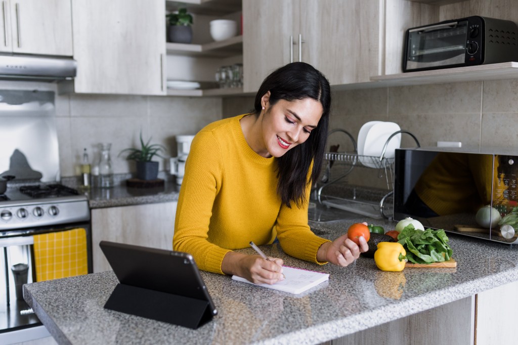 Latin adult woman cooking and writing recipe in a notebook in kitchen at home in Mexico, Hispanic female preparing mexican food in Latin America