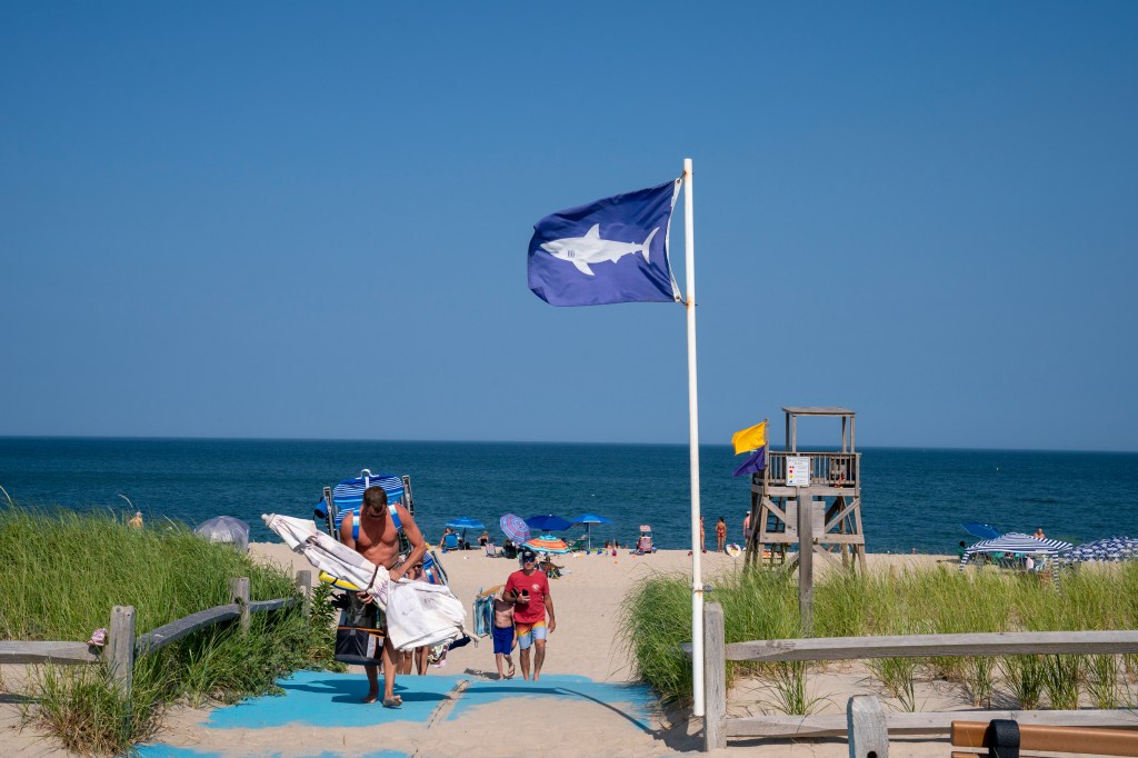 A flag with a shark warning flies as beachgoers depart July 26, 29023 at Nauset Beach in Orleans Massachusetts.