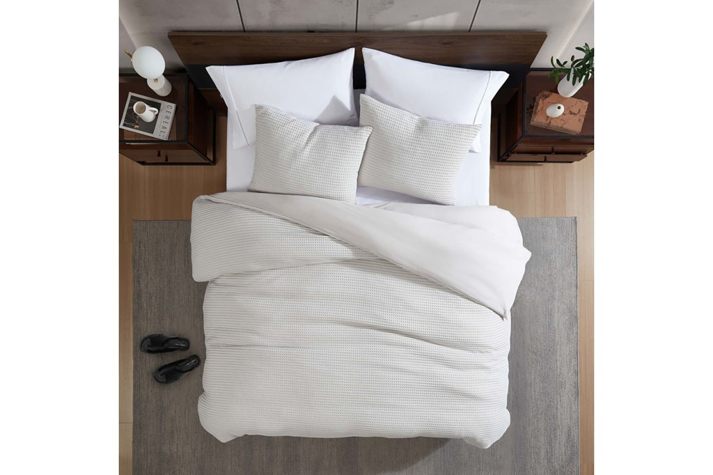 A bed with a white comforter and pillows from Kenneth Cole