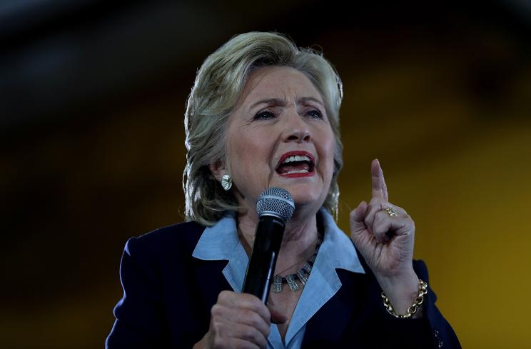 Hillary Clinton pointing with one hand and holding a microphone with another