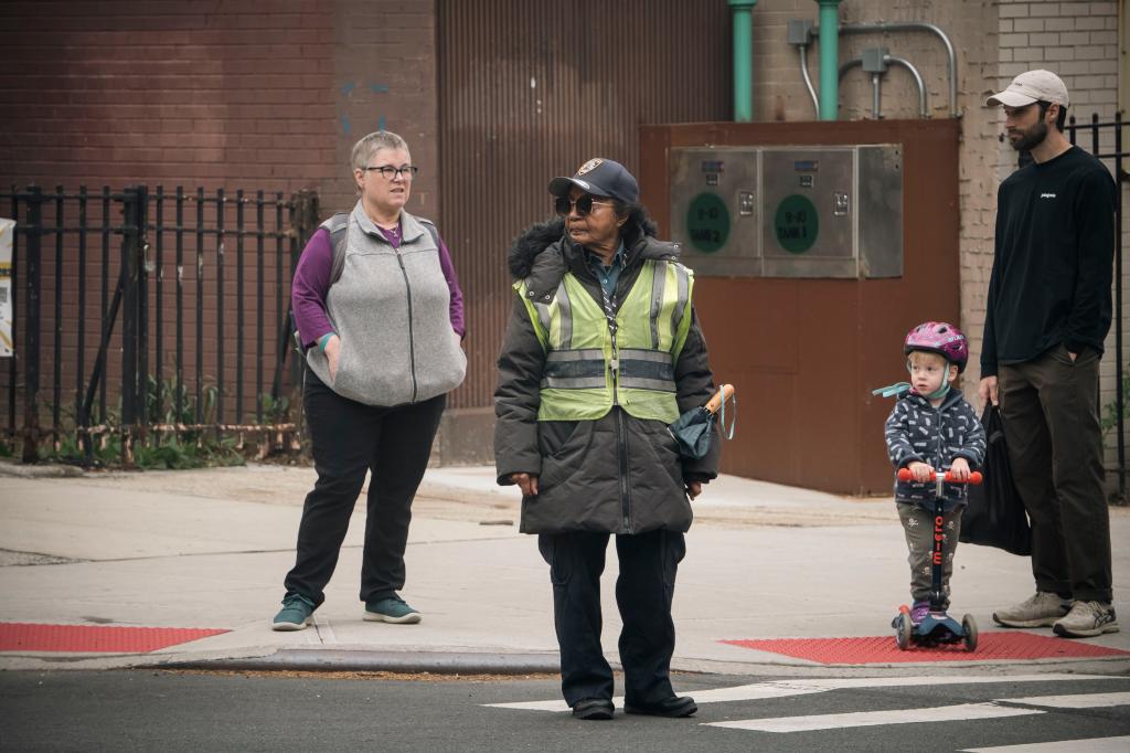 Maggie Poston stands on a Park Slope corner as two adults and a small child on scooter wait to cross. 