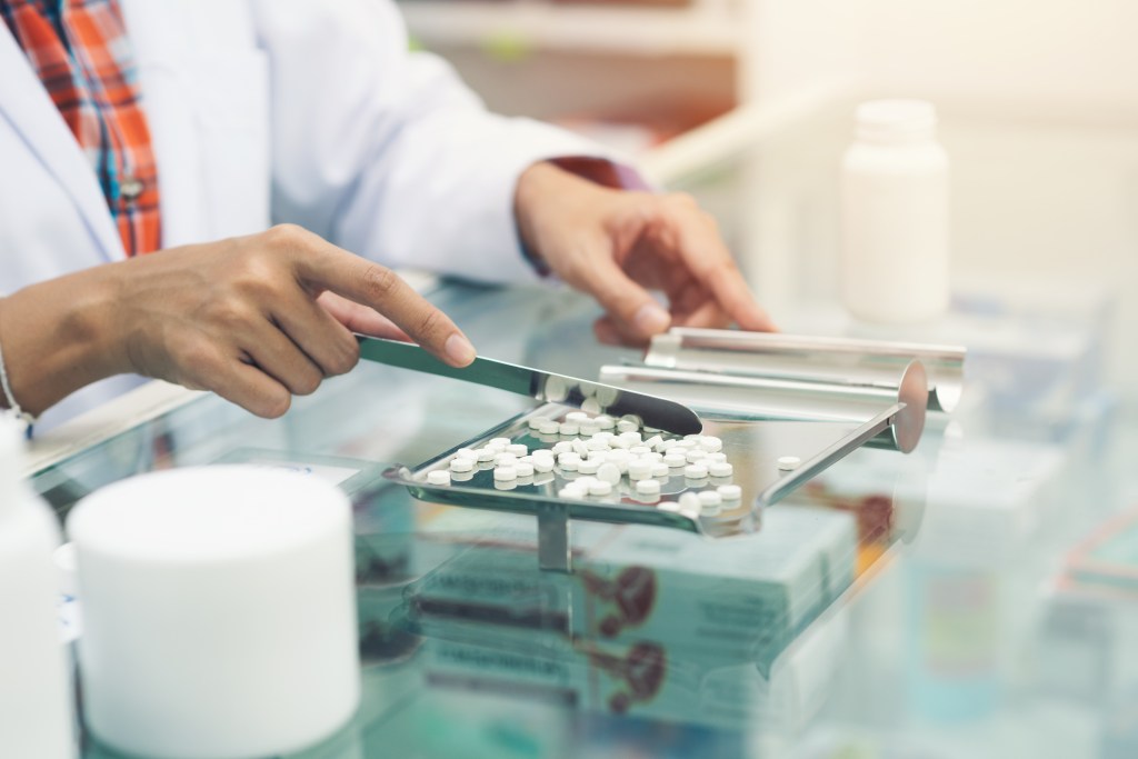 pharmacist with medication Medicine tablets on counting tray with counting spatula at pharmacy.