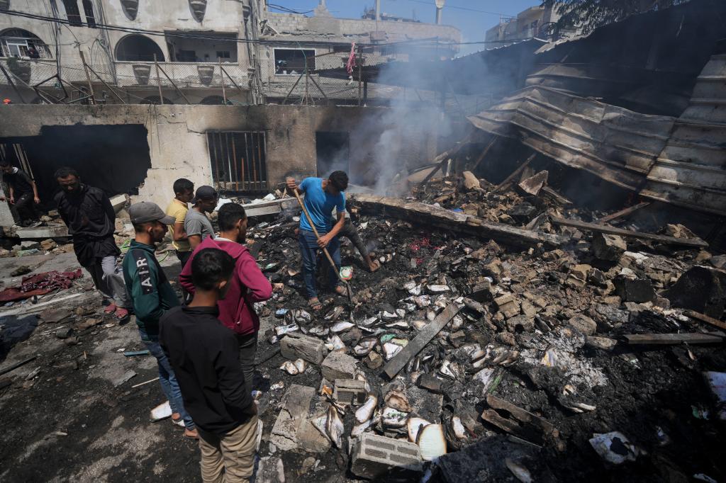 Onlookers watch a man sift through rubble with a shovel