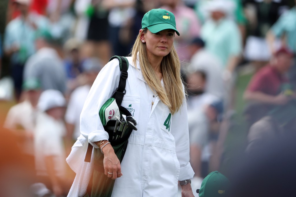 Erica Stoll in a green hat and white jumpsuit caddying for Rory McIlroy at the 2023 Masters Par 3 Contest, Augusta, Georgia