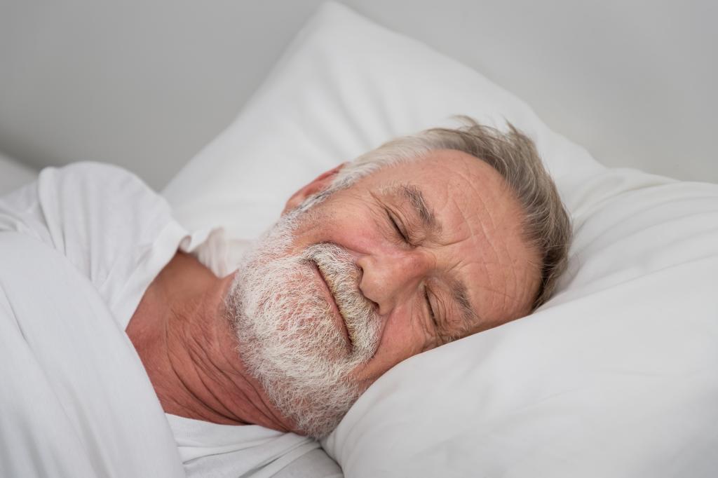 Senior elderly man sleeping happily with white blanket in bedroom
