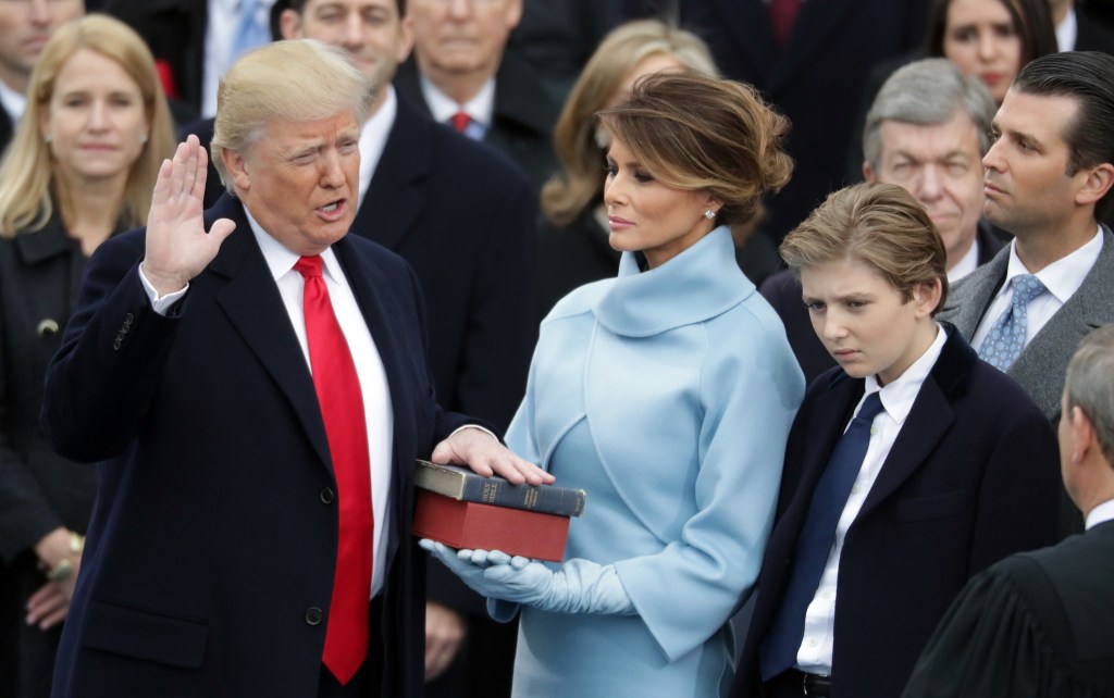 Donald Trump takes the oath of office as Melania Trump holds the Bible and Barron Trump looks on.