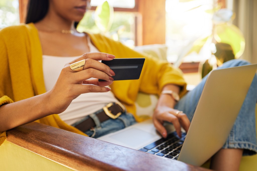 Closeup of a woman's hands using a credit card for online shopping on a laptop at home