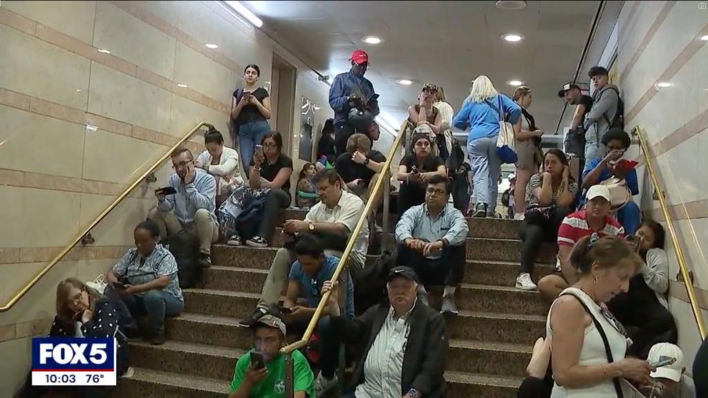 Commuters sit on stairs at New York's Penn Station as they wait out delays caused by downed wires in between Newark and New York.