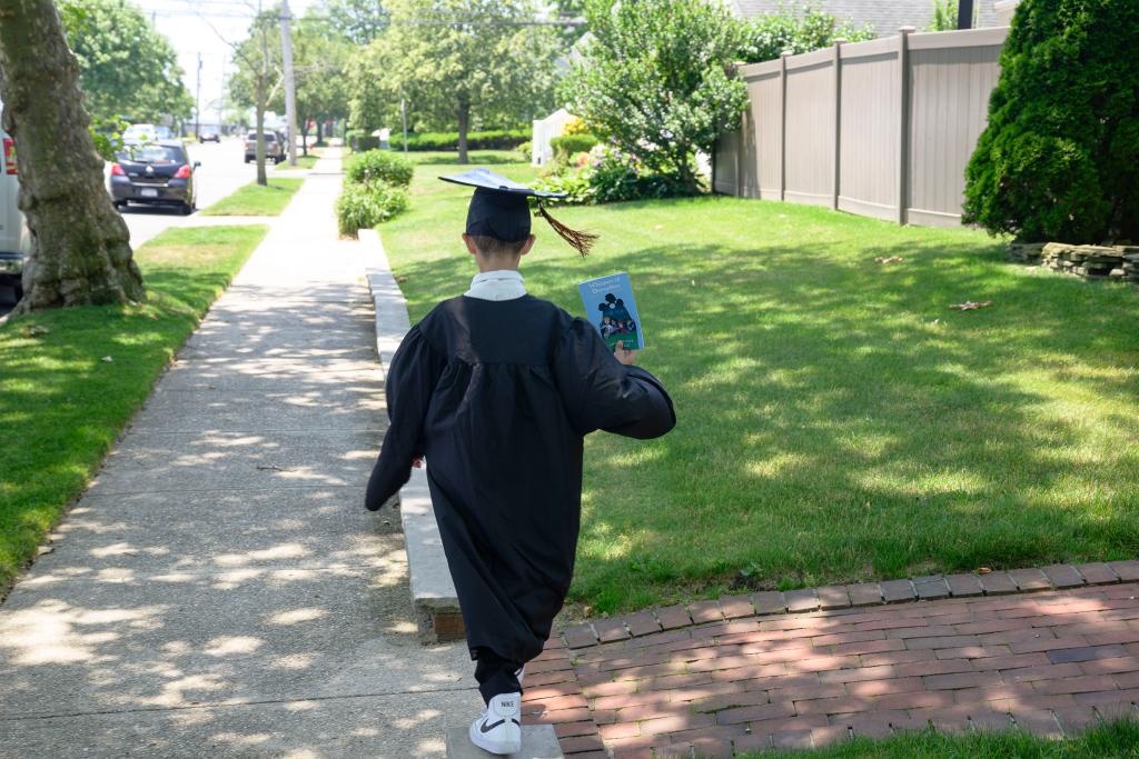 11-year-old Joe Petraro in a cap and gown holding one his books on the street