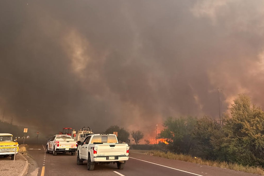 White trucks on a closed road due to the Rose Fire in Arizona, with a background of smoke and trees.