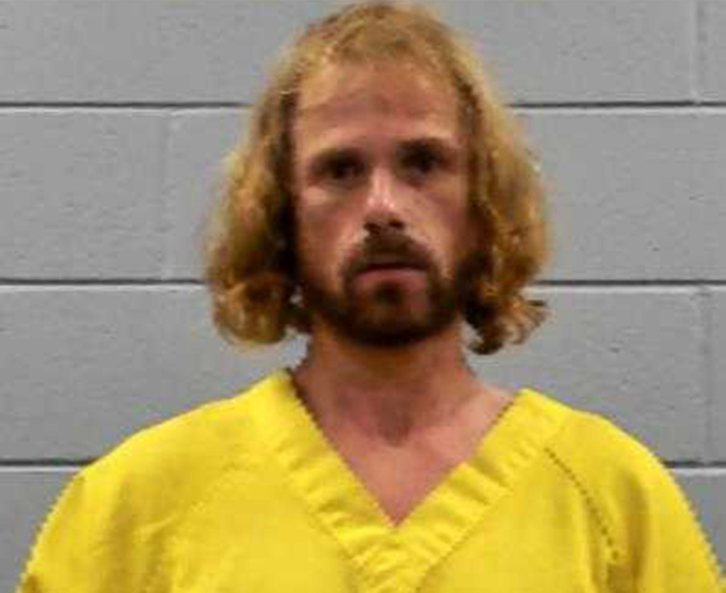 A booking photo of Daniel Callihan in a yellow prison jumpsuit, with long hair and beard.