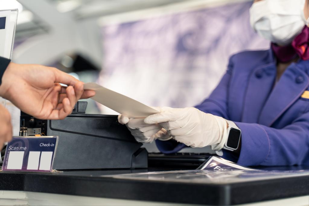 An Asian man receiving his boarding pass from a female airline officer wearing a face mask to prevent COVID-19 spread at the airport.