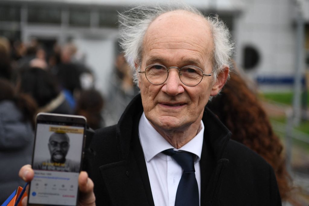 John Shipton, father of Julian Assange, holding up a smartphone displaying a support video for his son outside Woolwich Crown Court