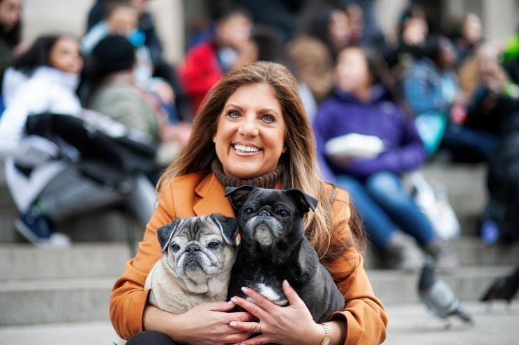 Amy Attas smiles and holds two pug dogs.