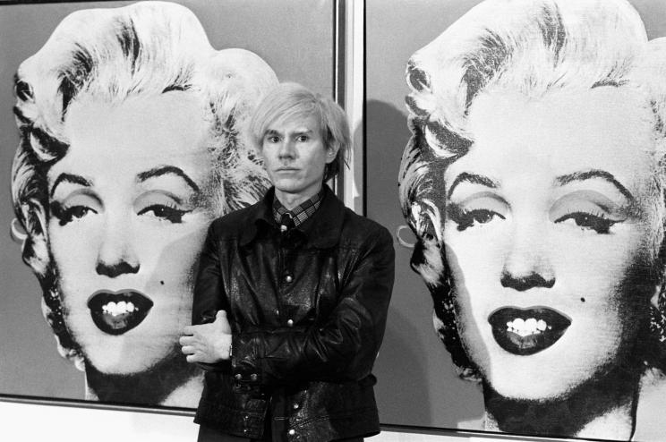 A photo of Warhol posing in front of his screenprints of Marilyn Monroe.