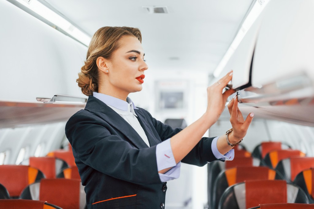 Young stewardess deals with overhead bin.