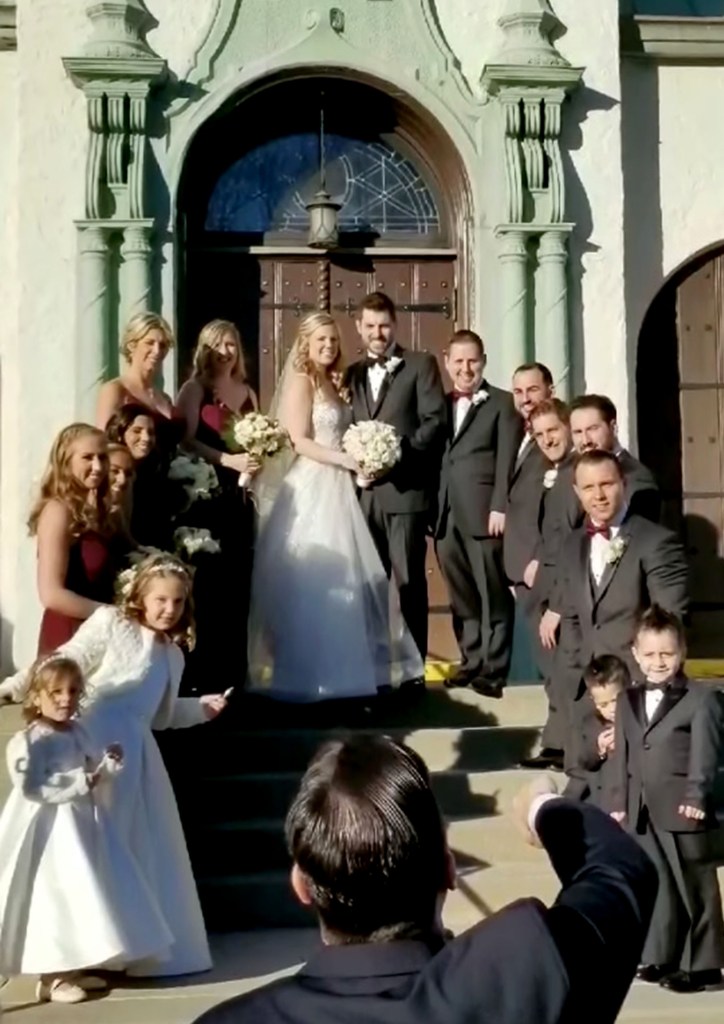 The wedding party stands on church stairs.