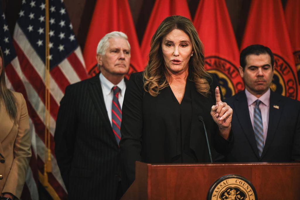 Caitlyn Jenner, former Olympic gold medalist, speaking at a podium about trans athlete legislation while Nassau County Executive Bruce Blakeman stands in the background