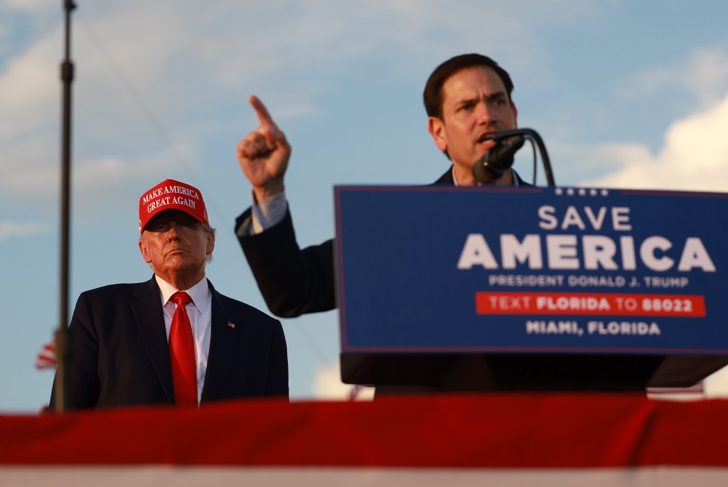 Former President Donald Trump attentively listening to Senator Marco Rubio speaking at a rally in Miami, Florida