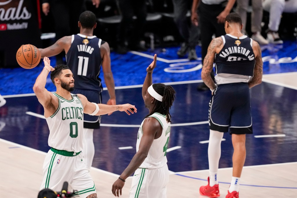 Boston Celtics forward Jayson Tatum (0) and guard Jrue Holiday react as Dallas Mavericks guard Kyrie Irving (11) and forward P.J. Washington walk off away after the Celtics won 109-66 in Game 3 of the NBA basketball finals, Wednesday, June 12, 2024, in Dallas.