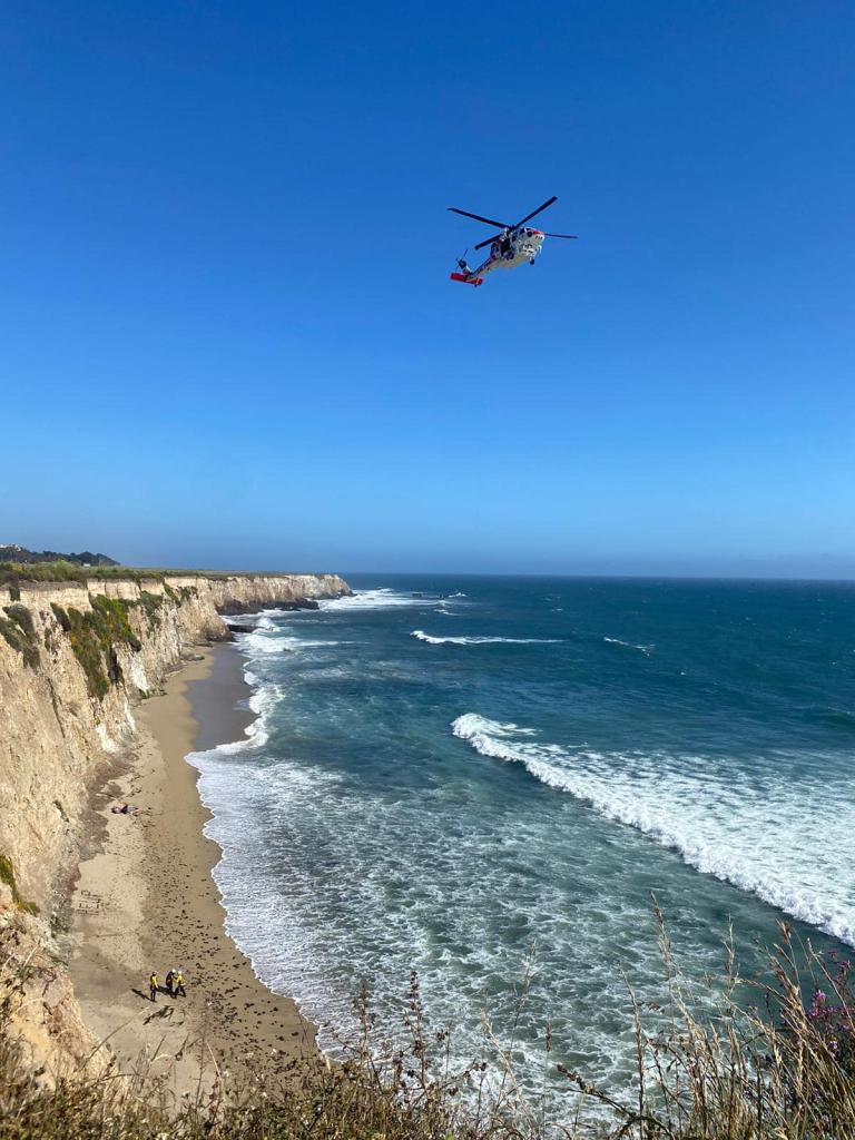 A helicopter flying over a beach to rescue a stranded kite surfer who spelled out 'HELP' with rocks on the beach