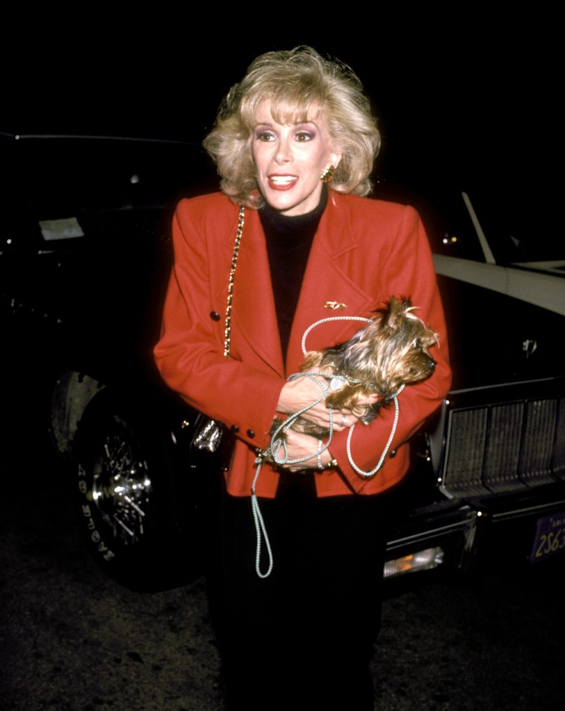 Joan Rivers outside Spago in Beverly Hills in 1986. She wears a red jacket and holds a small Yorkshire terrier. 