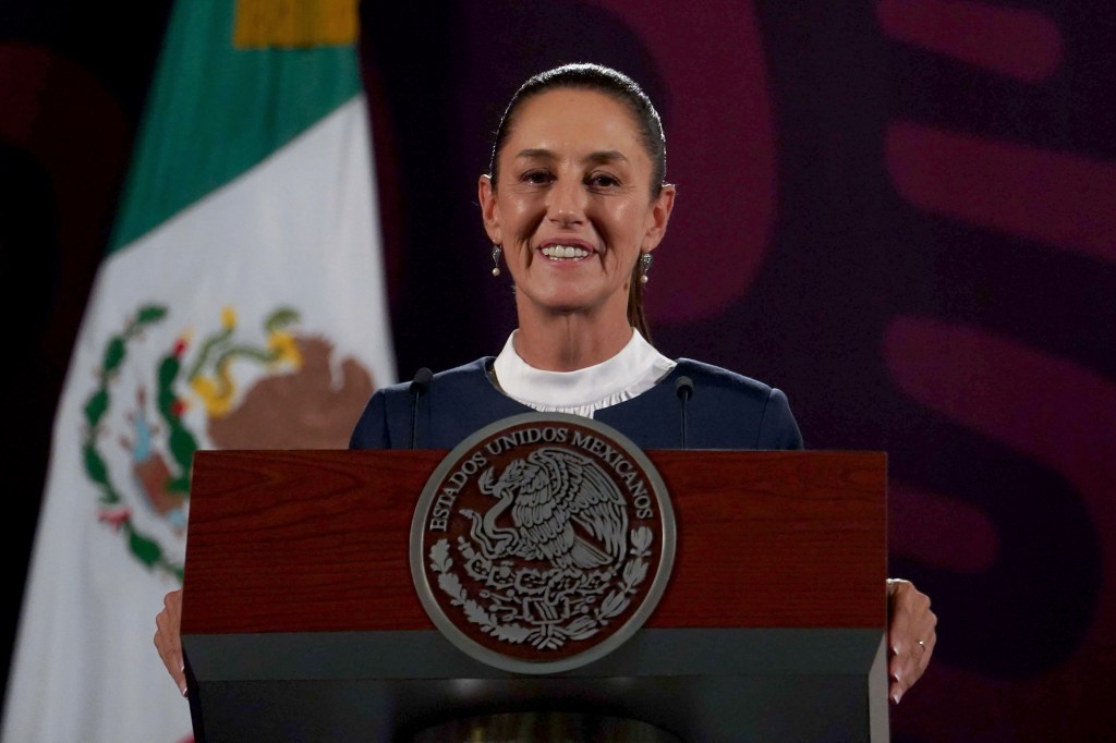 Claudia Sheinbaum standing at a podium with Mexico's flag behind her