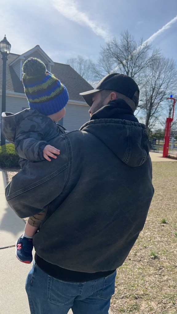 Diller walking into the park with his son on his shoulders.