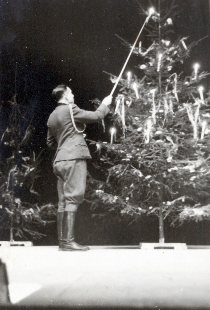 A uniformed Nazi lights a yule Christmas tree. A chilling photo album shows Nazis at Auschwitz enjoying blueberries and sunbathing in deckchairs. The candid moments were captured on camera as 1.1 million people were murdered at the death camp. The album was found by an unnamed American counterintelligence officer who was billeted in Frankfurt after Germany's surrender in 1945. The photos are now the subject of a play that opened last month off-broadway, the 2024 Pulitzer Prize for Drama finalist Here There Are Blueberries. The play dramatises the work of the curators who examined the mysterious album featuring the Nazi-era photographs that arrived at the desk of a U.S. Holocaust Memorial Museum  (USHMM) archivist in 2007. The album consists of 116 photographs taken during the last six months of Auschwitz, between June 1944 and January 1945. The album shows Auschwitz during its most lethal period, coinciding with the murder of 400,000 Hungarian Jews.