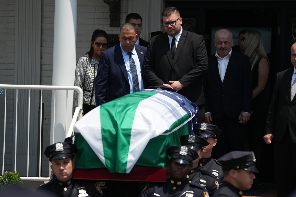 The husband and family walking out of funeral home behind casket.